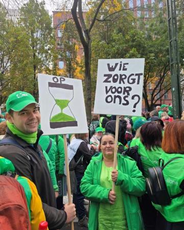 Een foto van betogers die in het groen gekleed zijn, ze dragen pancartes waar op te lezen staat 'wie zorgt er dan voor ons?'