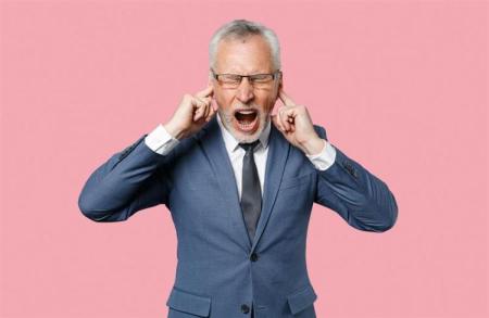 Oudere man in een pak die zijn vingers in zijn oren steekt